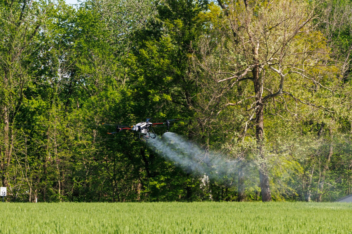 DJI Agras spray drone applying product along a tree line
